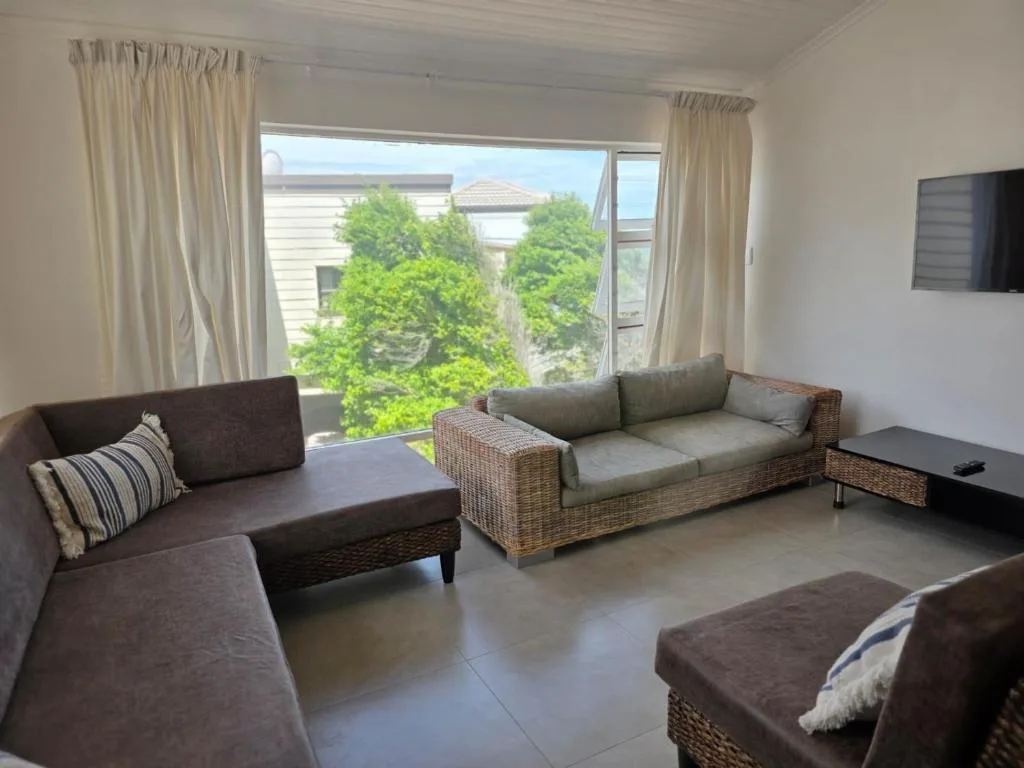 Modern lounge with multiple sofas, TV, and large windows overlooking garden