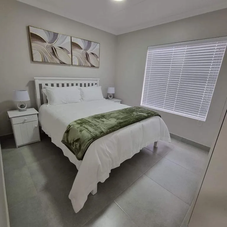 Bright bedroom with white bed, green throw, and large window blinds