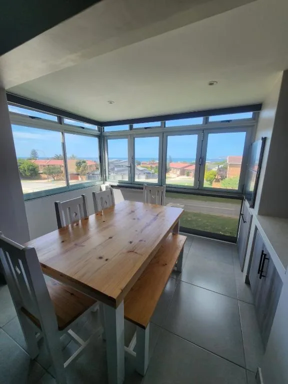 Bright dining area with wooden table and panoramic windows overlooking coastal landscape