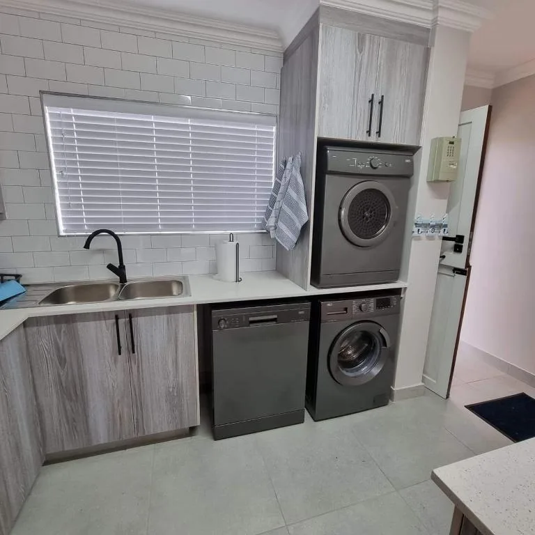 Modern laundry room with dual washing machines, sink, and storage cabinets