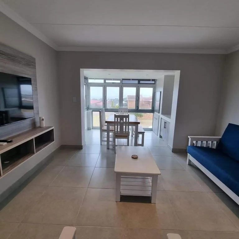 Open-plan lounge with TV, sofa, and dining area beyond glass doors
