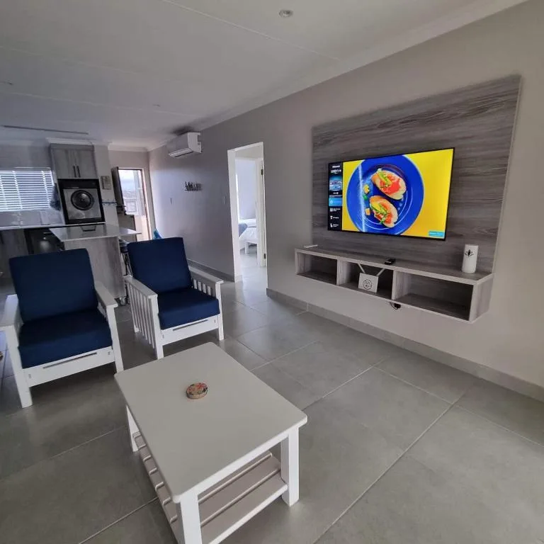 Modern living room with wall-mounted TV, white furniture, and blue cushions