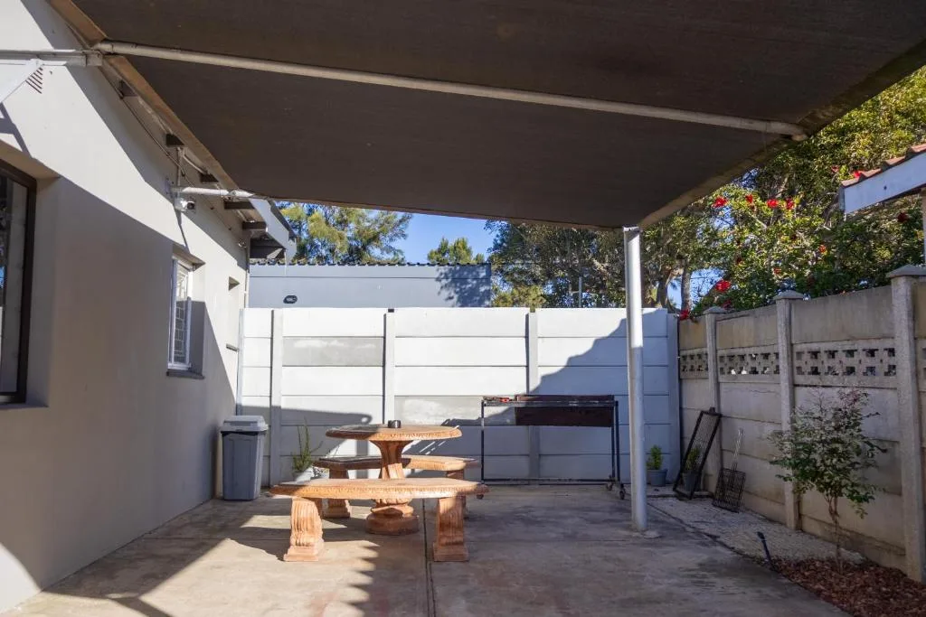 Shaded patio with picnic tables, braai grill, and garden seating area