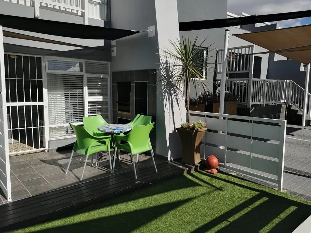 Modern patio with green chairs, table, shade sails, and potted plants