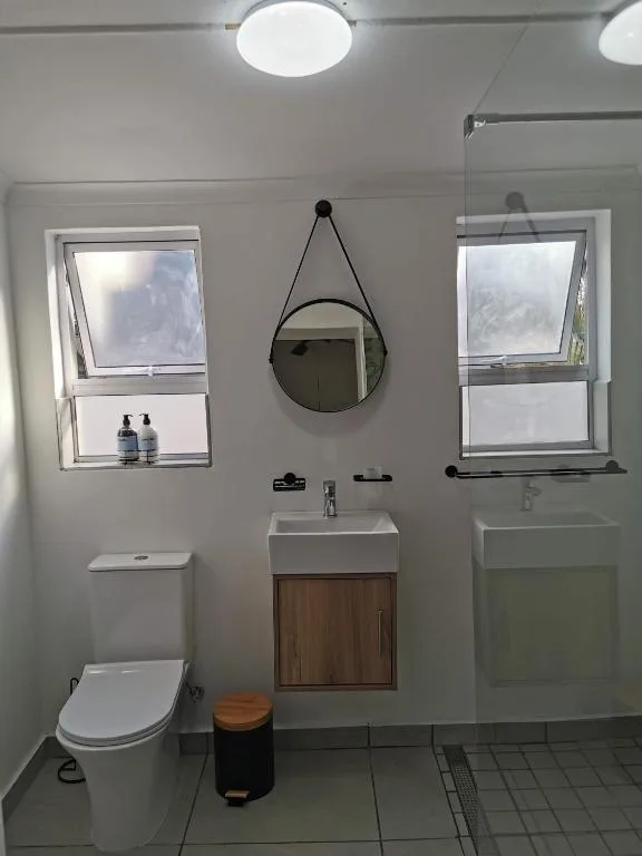 Modern bathroom with toilet, vanity sink, round mirror, and bright windows