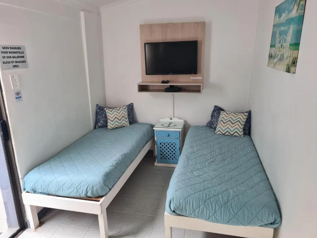 Twin bedroom with blue quilts, TV mounted on wall, shared nightstand