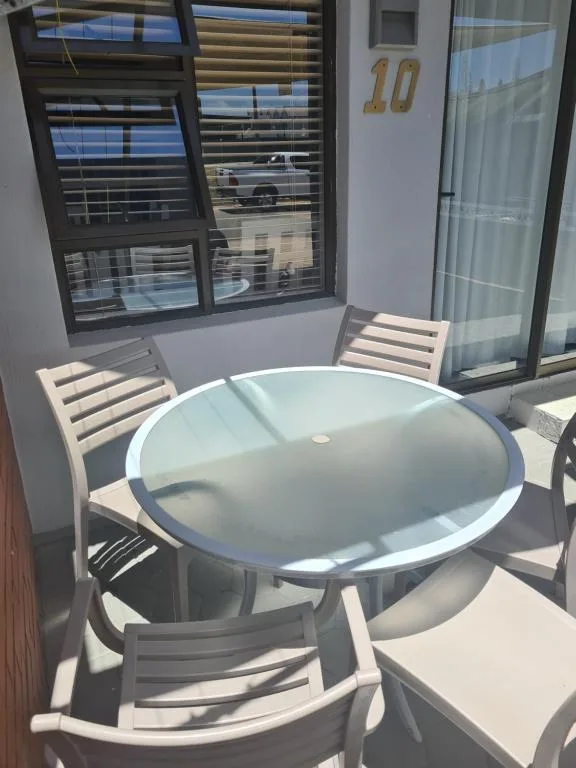 Round glass table with white chairs on sunny outdoor patio area