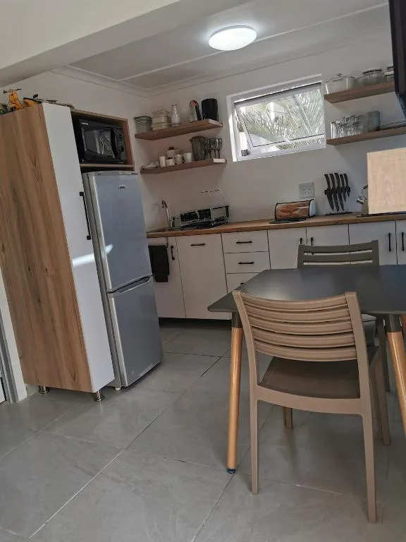 Modern kitchen with stainless steel fridge, wooden cabinetry, open shelving, and dining chair