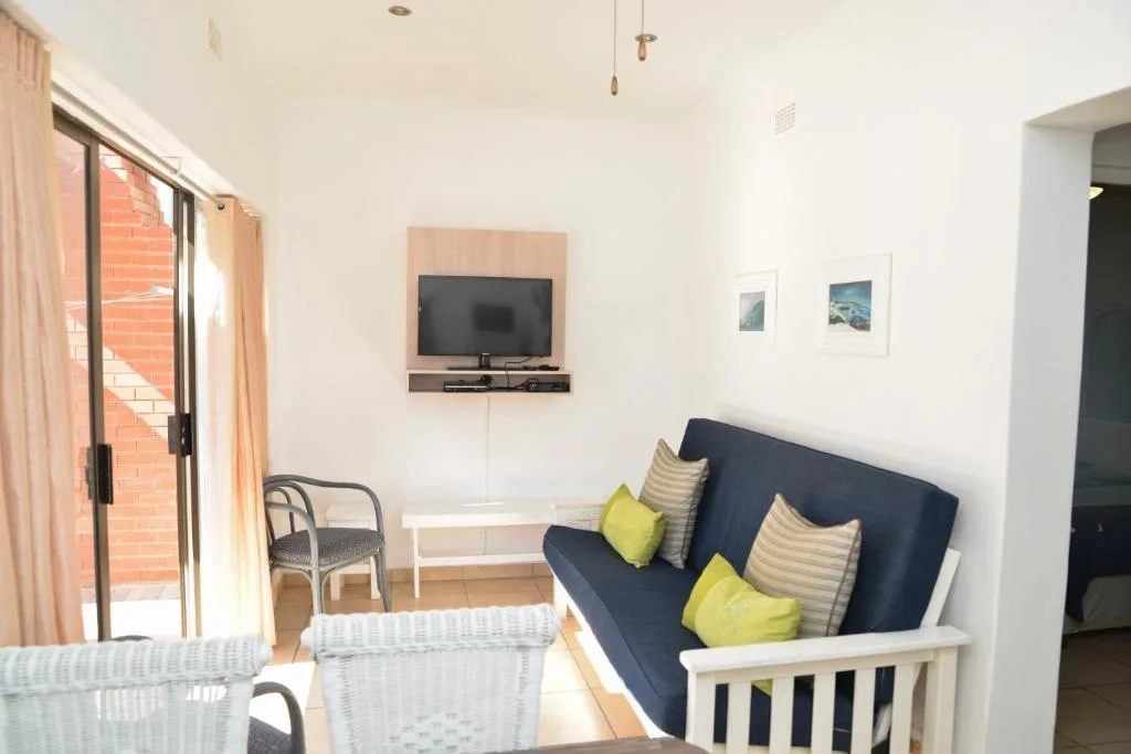 Living room with dark blue sofa, yellow cushions, wall-mounted TV, and glass doors