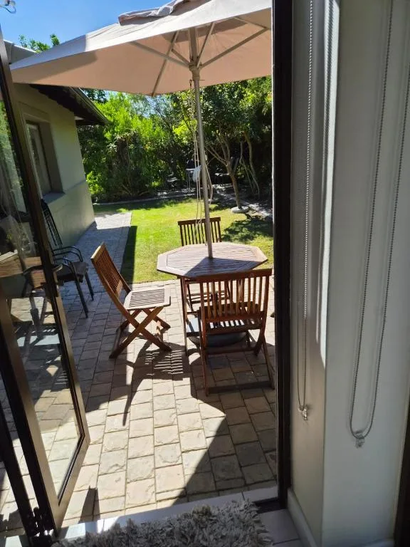 Outdoor patio with round table, wooden chairs, and large umbrella shading