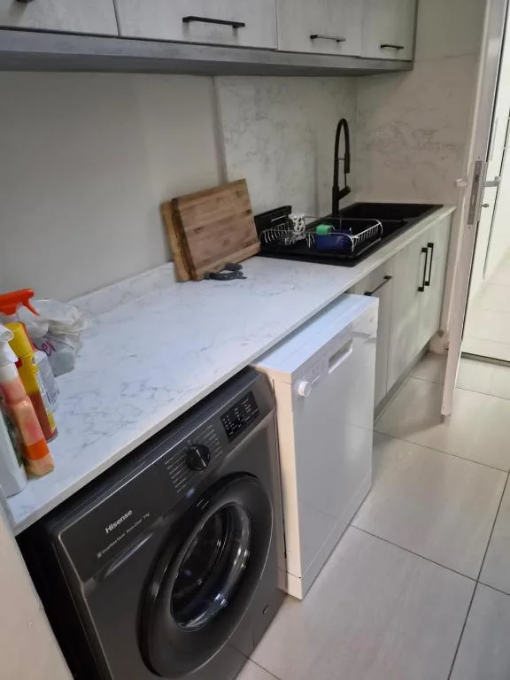 Modern kitchen with marble countertop, sink, washing machine, and cabinetry