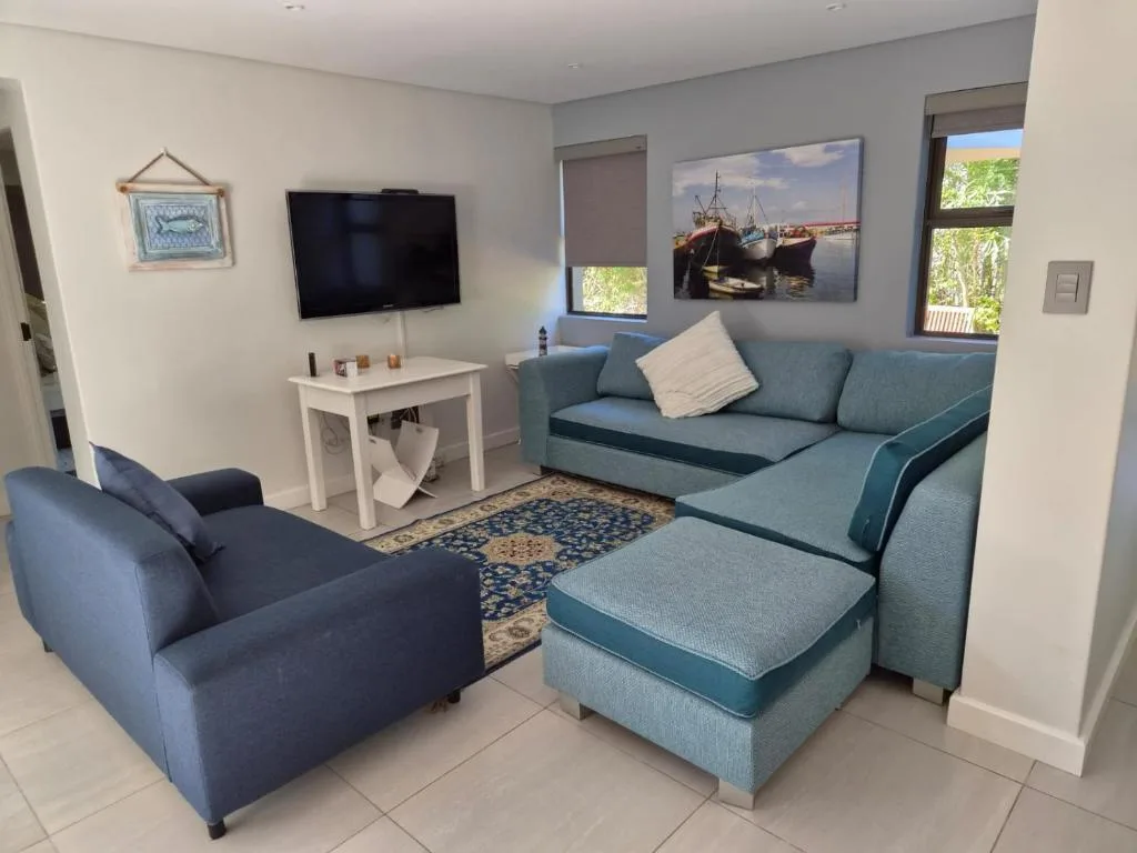 Spacious lounge with blue sofas, armchair, TV, and harbor artwork