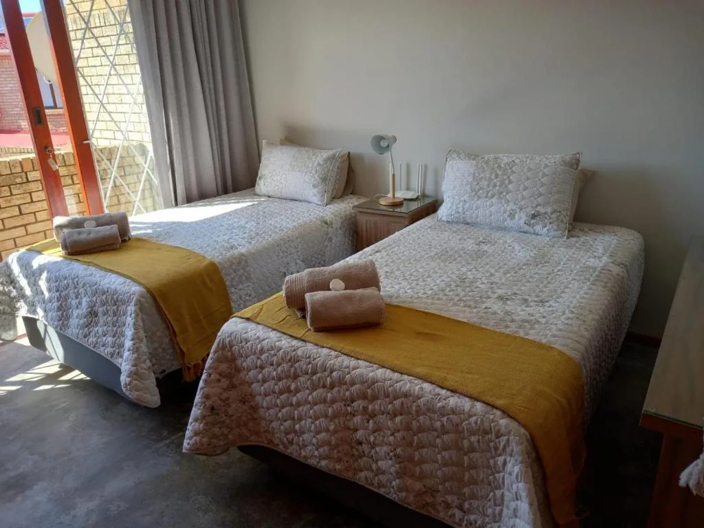 Twin bedroom with patterned quilts, mustard throws, and natural light