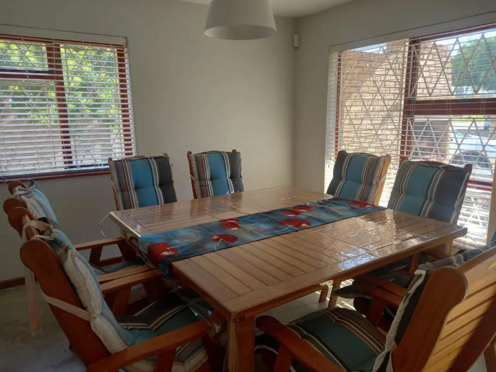 Bright dining area with wooden table and striped blue chairs, large windows with blinds