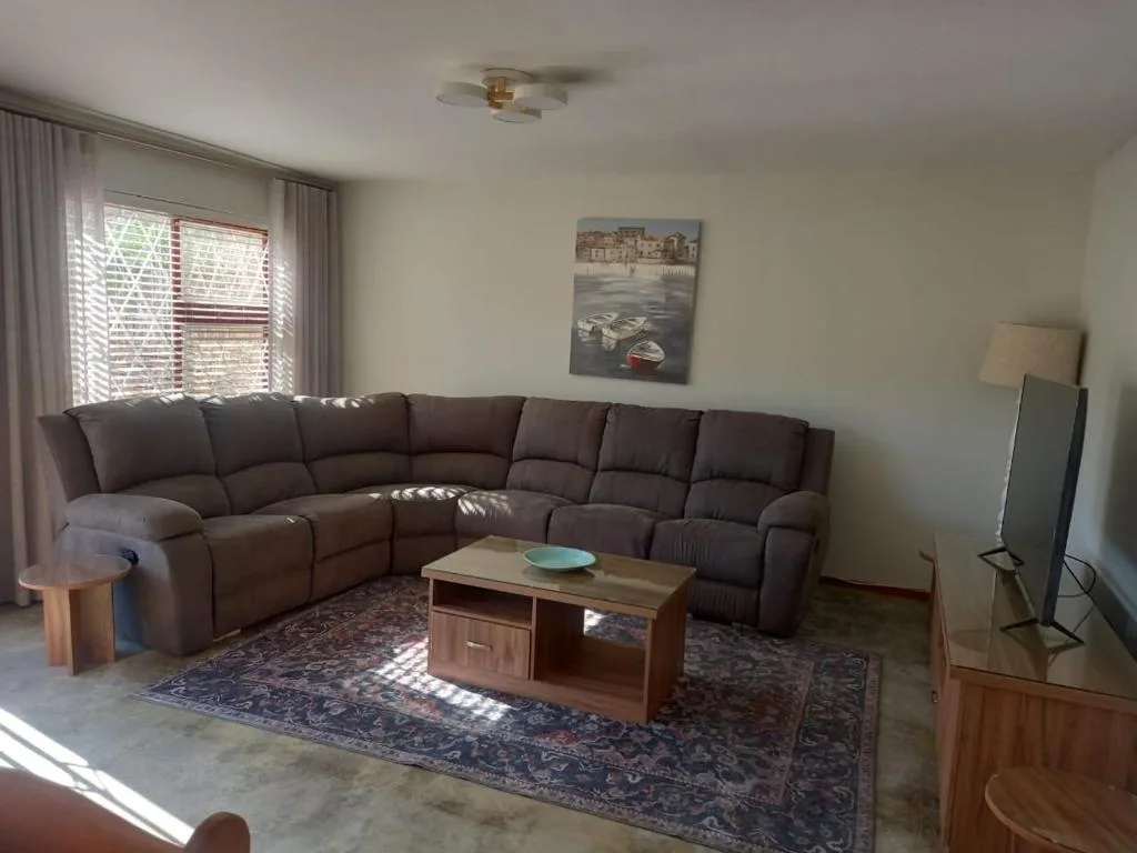 Spacious lounge with brown sectional sofa, wooden coffee table, and coastal artwork