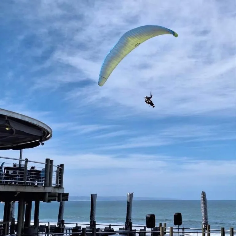 Paraglider soaring above beachfront deck with ocean horizon view