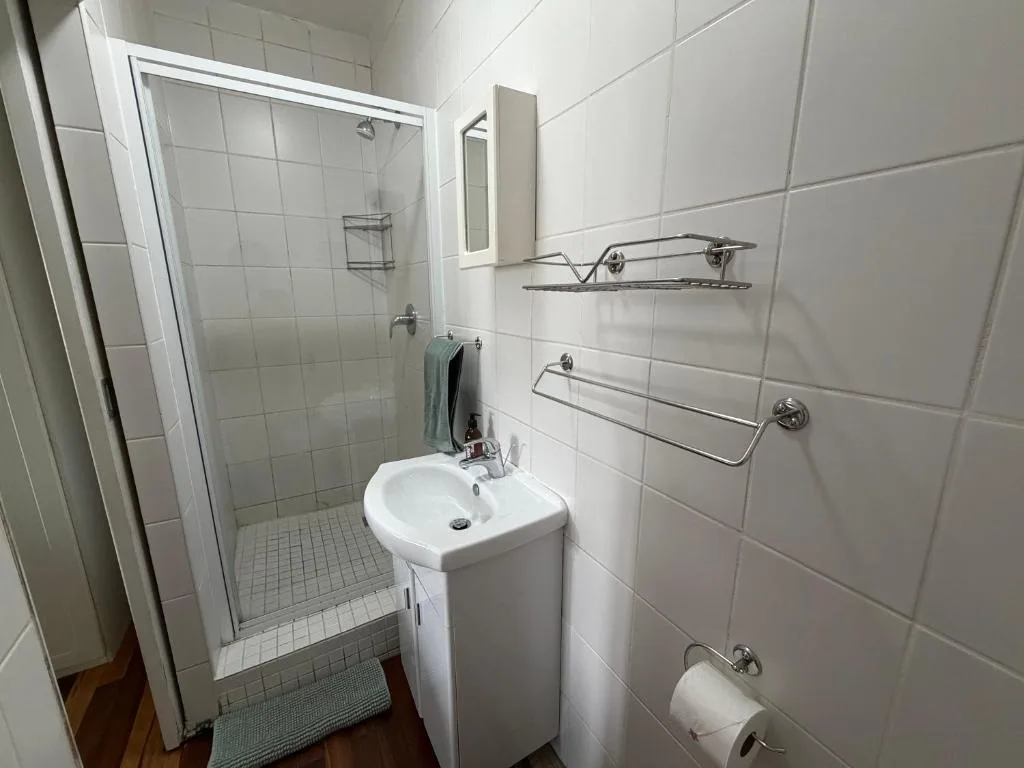 Clean white tiled bathroom with shower, sink vanity, and towel rails