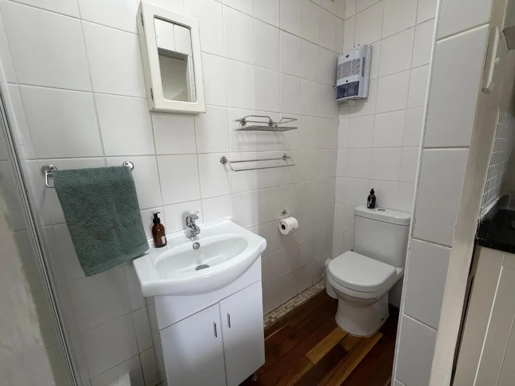 Clean bathroom with white tiles, vanity sink, toilet, and towel rack