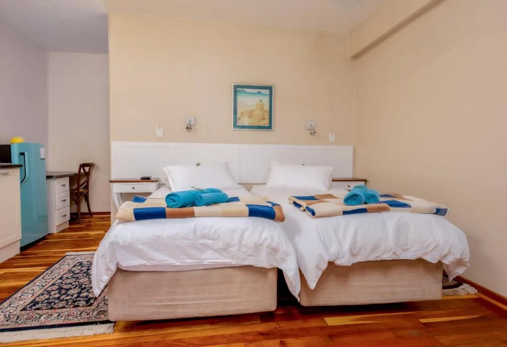 Spacious bedroom with two twin beds, white pillows, blue towels, wooden floors