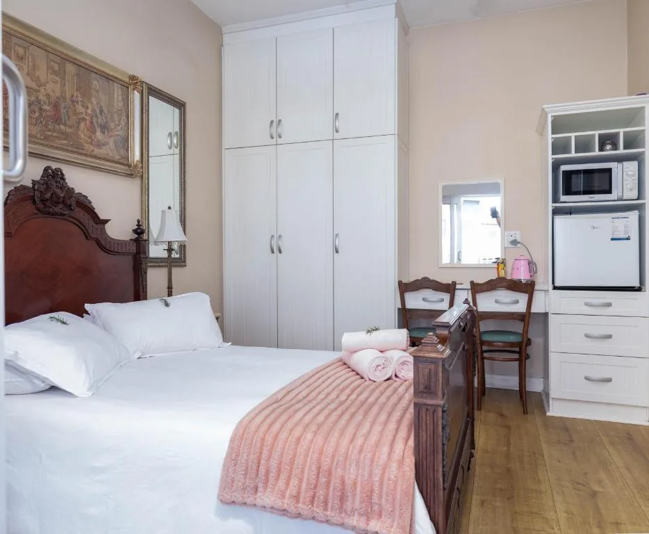 Bright bedroom with wooden bed, white linens, pink blanket, and built-in wardrobe