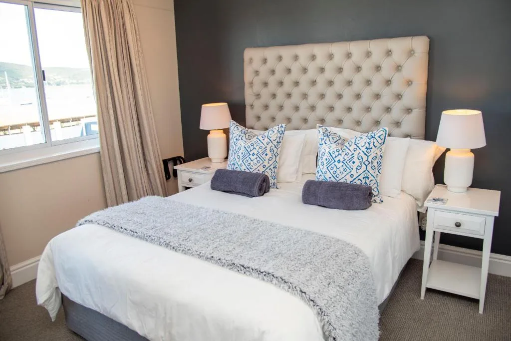 Modern bedroom with upholstered headboard, white bedding, and waterfront view through window