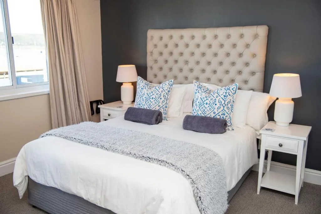 Spacious bedroom with upholstered headboard, white bedding, and ocean view windows