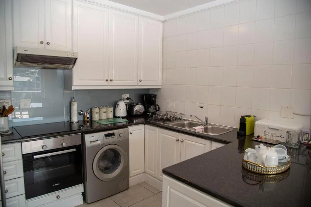 Modern white kitchen with black countertops, oven, and washing machine