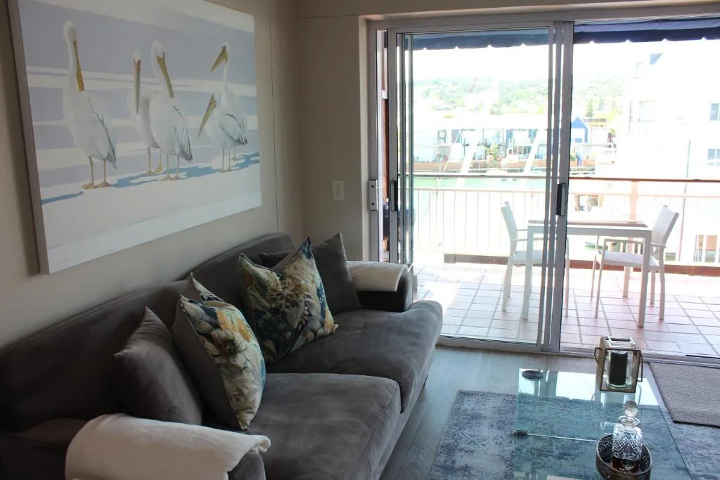 Modern lounge with gray sofa, bird artwork, and sliding doors opening to waterfront deck