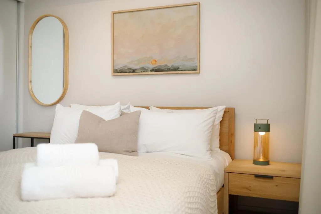 Bright bedroom with wooden bed frame, white pillows, and minimalist wall art