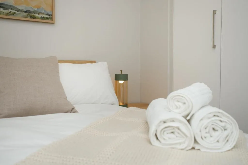 Neatly made bed with rolled towels and modern bedside lamp