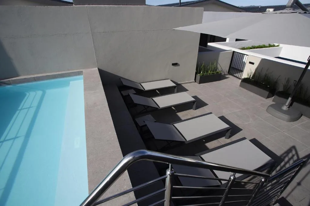 Modern patio with loungers, pool, and white shade structures overlooking water