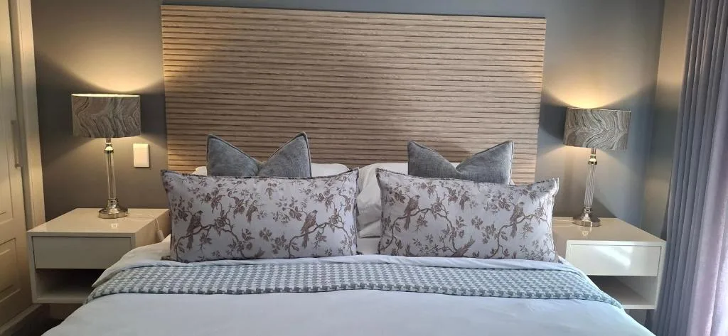 Modern bedroom with queen bed, floral pillows, wooden headboard, bedside lamps