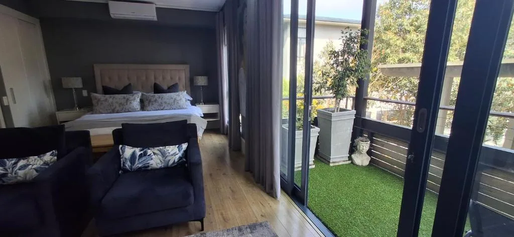 Modern bedroom with bed, armchair, and balcony access overlooking greenery