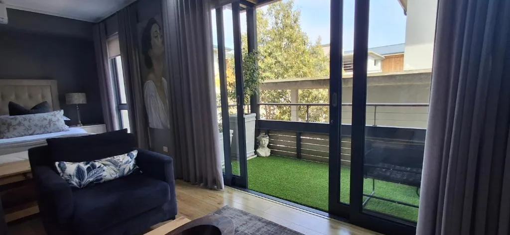 Modern bedroom with bed, armchair, and glass doors opening to deck with artificial turf