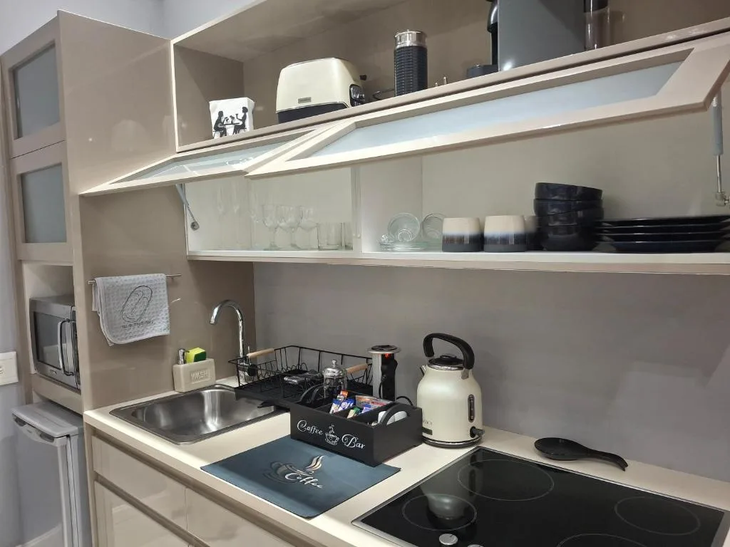 Modern kitchenette with electric cooktop, sink, and open shelving displaying tableware