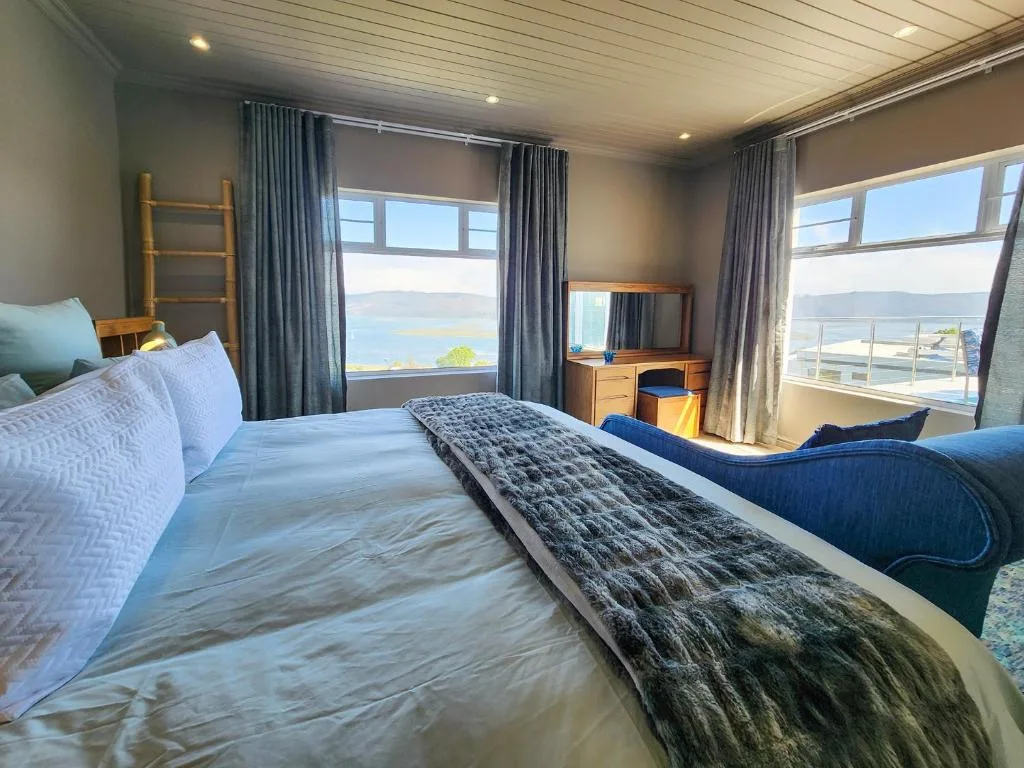 Bright bedroom with water view, blue curtains, wooden furniture, and natural light