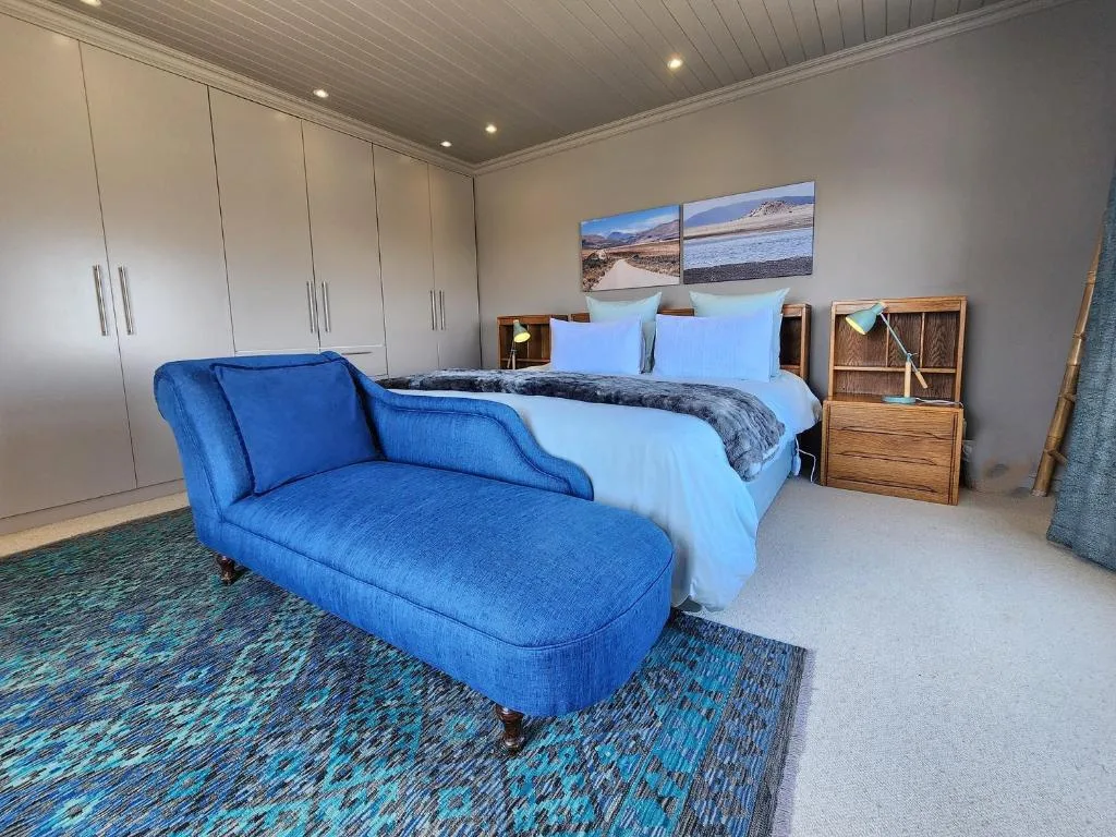 Modern bedroom with queen bed, blue chaise lounge, and built-in wardrobes