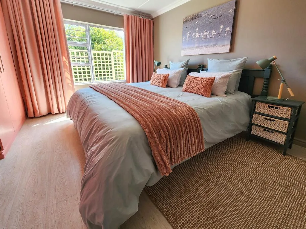 Bright bedroom with queen bed, coral bedding, and garden views through large windows