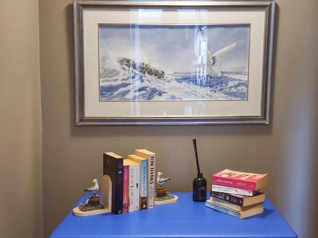 Framed aerial artwork and decorative books with bird bookends on blue shelf