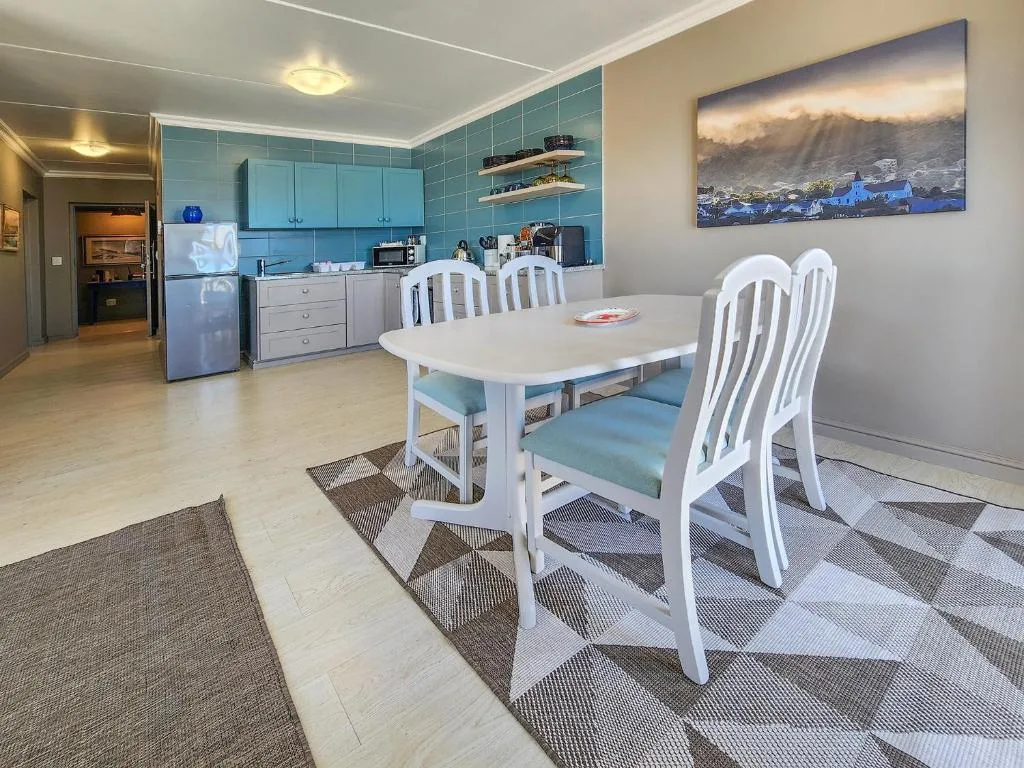 Open-plan dining area with white chairs and kitchen visible in background