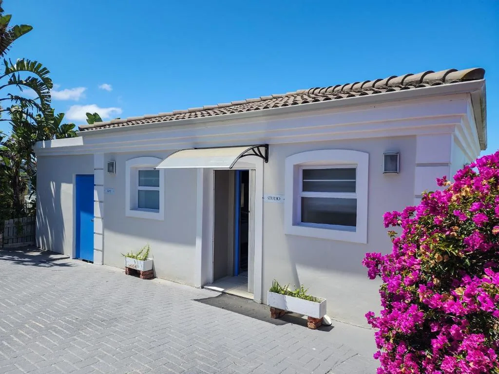 White studio apartment with blue door and vibrant magenta bougainvillea flowers