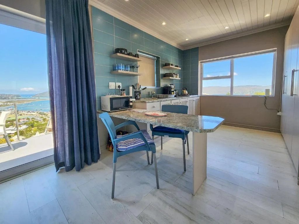 Modern kitchen with granite countertop, blue chair, teal tile backsplash, scenic lagoon view