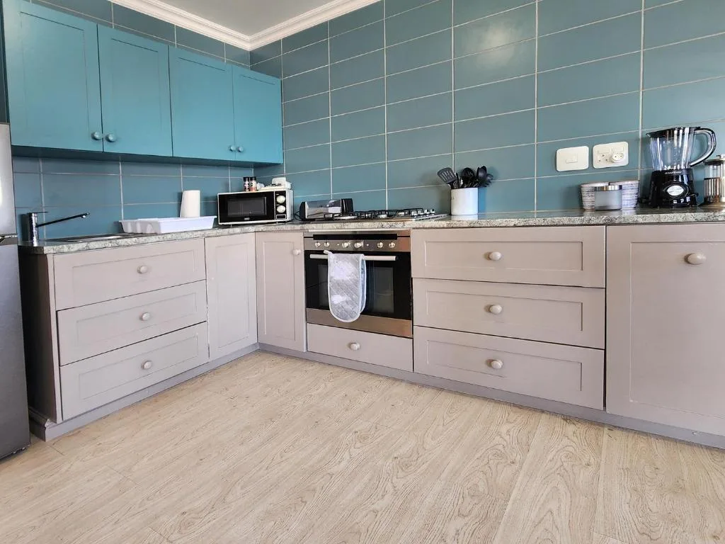 Modern kitchen with turquoise tiled walls, light cabinetry, and stainless steel appliances