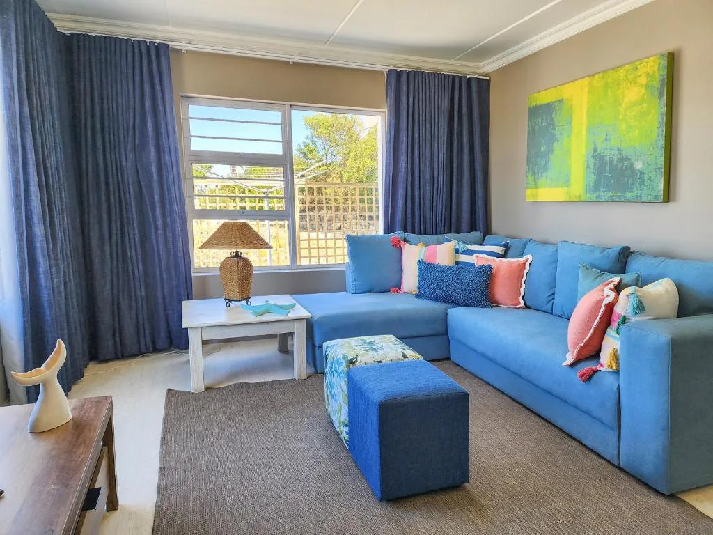 Bright lounge with blue sectional sofa, colorful cushions, and deck views