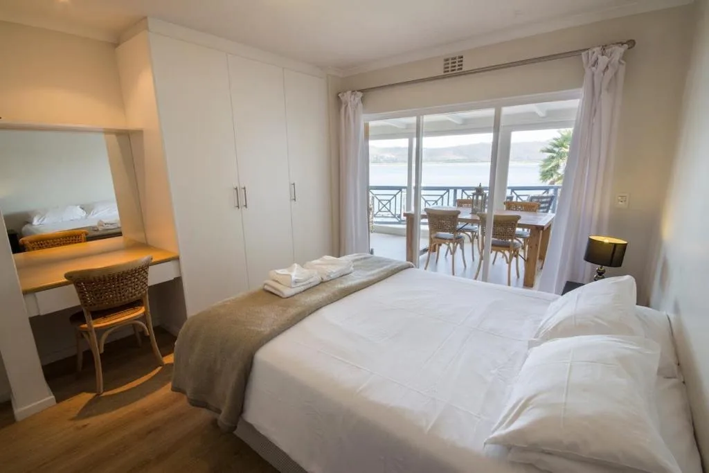 Spacious bedroom with white bed, desk, and lagoon views through glass doors