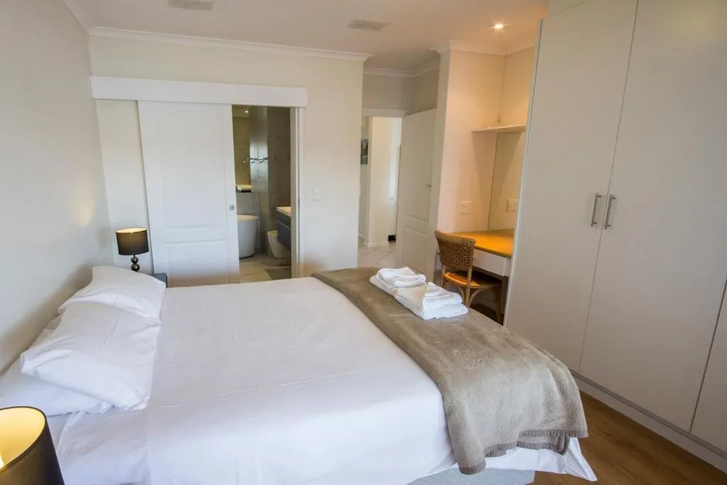Modern bedroom with white bed, en-suite bathroom visible, and built-in wardrobe storage
