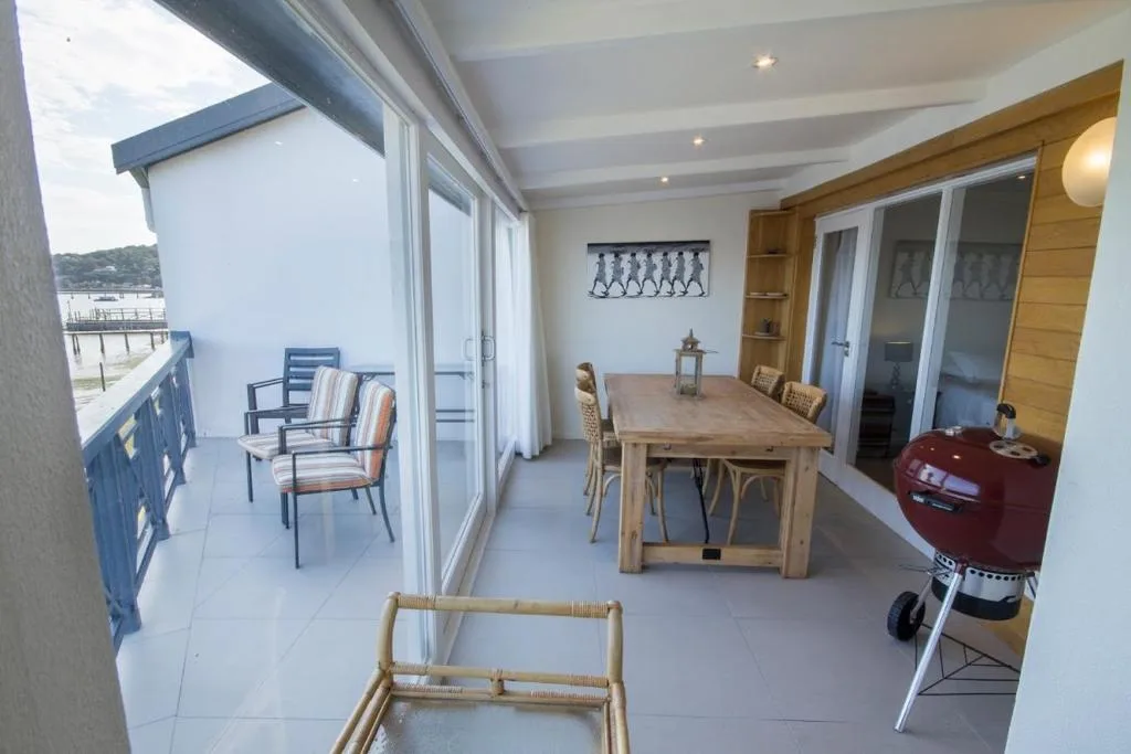 Spacious deck with dining table, seating area, and braai grill overlooking lagoon