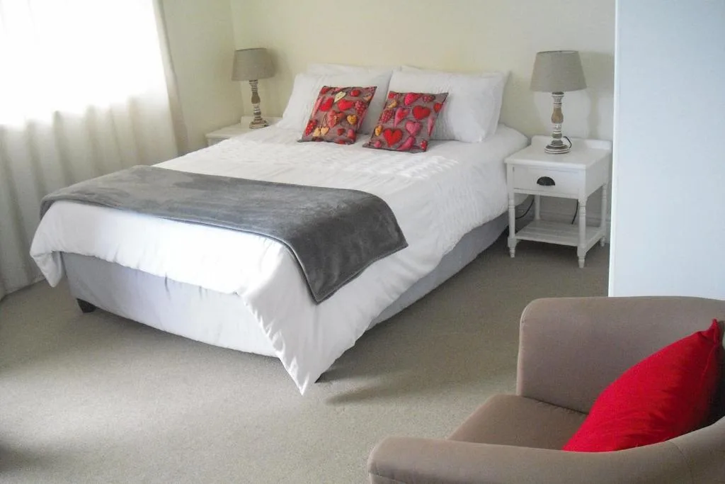 Bright bedroom with queen bed, white linens, floral pillows, and side tables