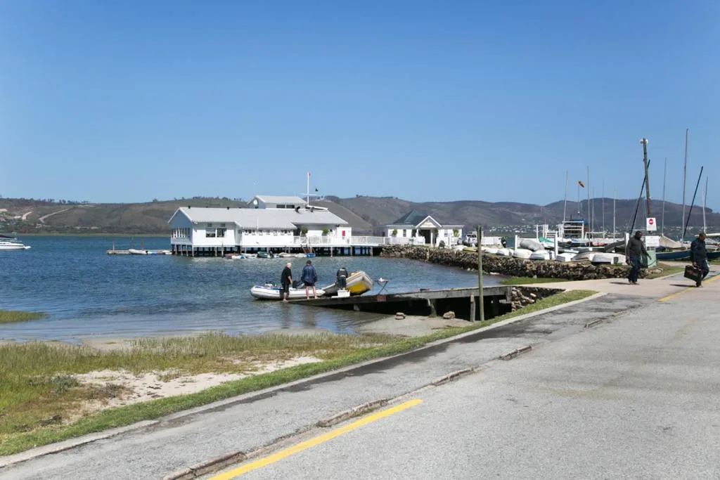 Waterfront harbor with white boathouse, moored boats, and surrounding hills