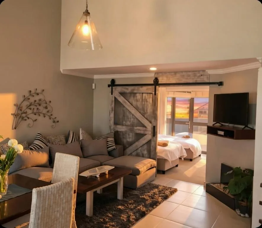 Open-plan lounge with gray sofa, TV, and sunset view through glass doors